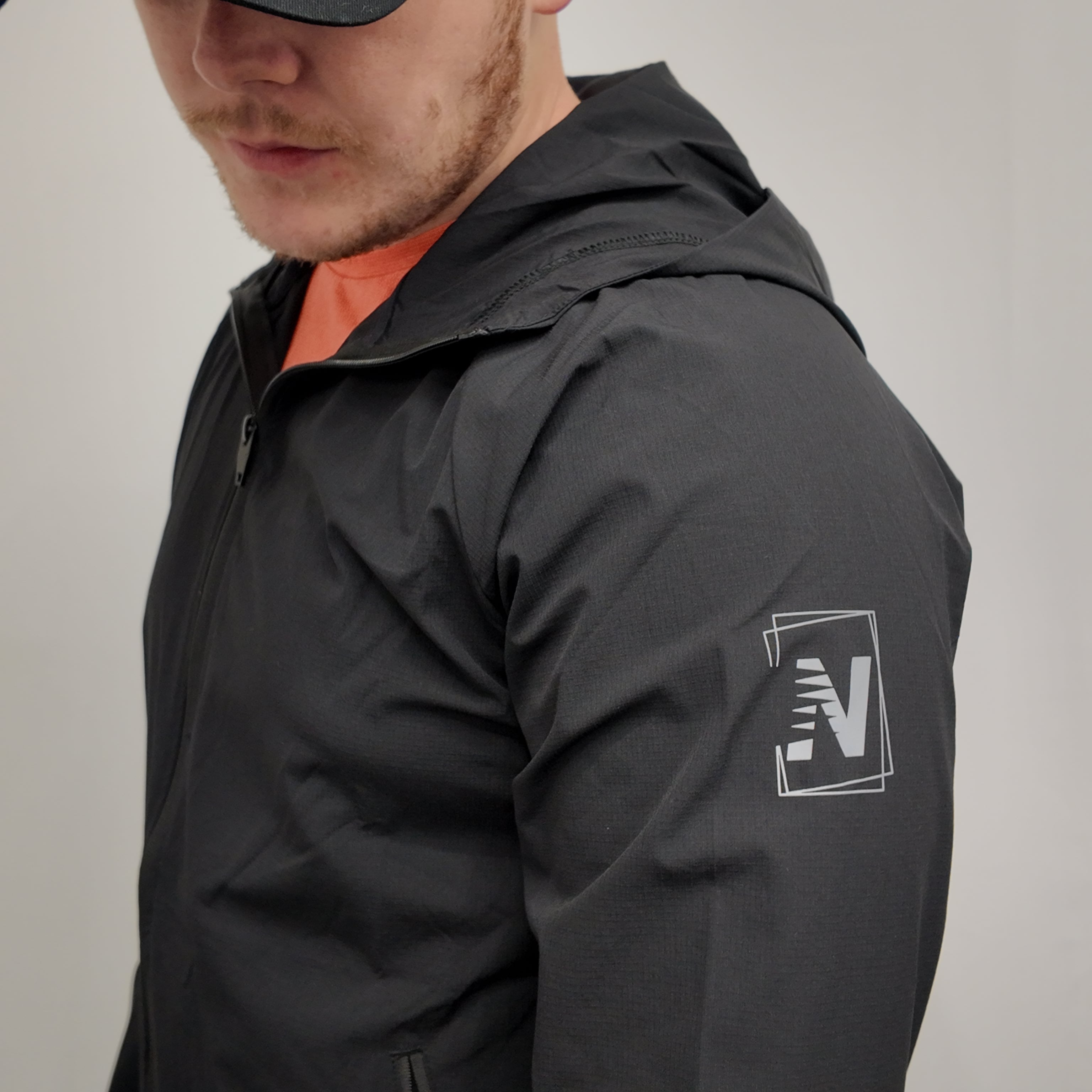 Translation missing: en.Person wearing a black jacket with a logo on the sleeve against a neutral background: NVSN Activewear